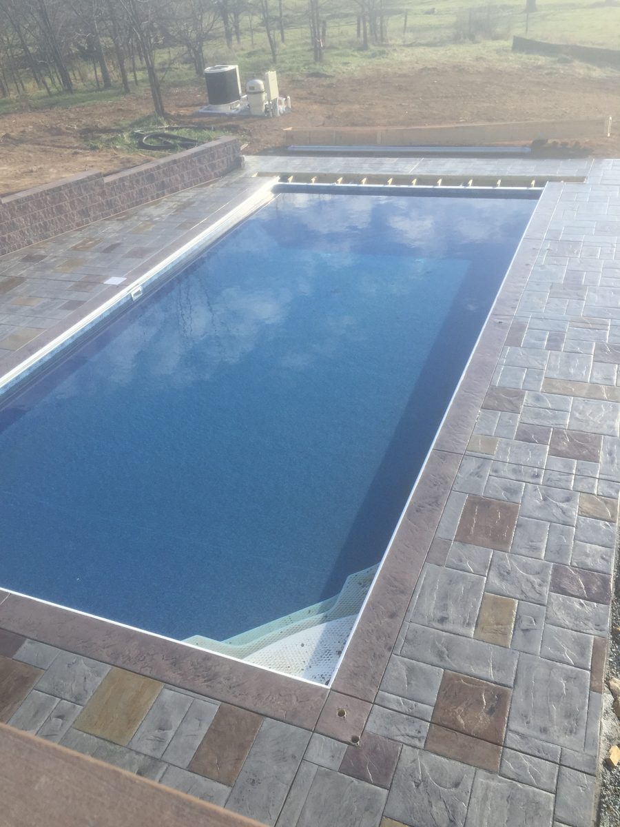Rectangular pool with a stamped concrete deck and stone look coping by Blackwater Designer Concrete